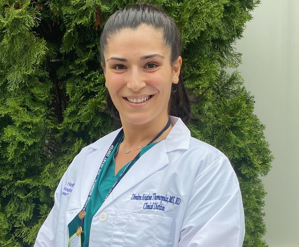 Krissi Thomopoulos, a PhD student in the Department of Nutrition Sciences, is wearing a white lab coat and green scrubs.